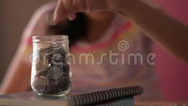 穿着休闲装的<strong>小</strong>女孩把钱放进<strong>一个玻璃</strong>罐子里接受教育。